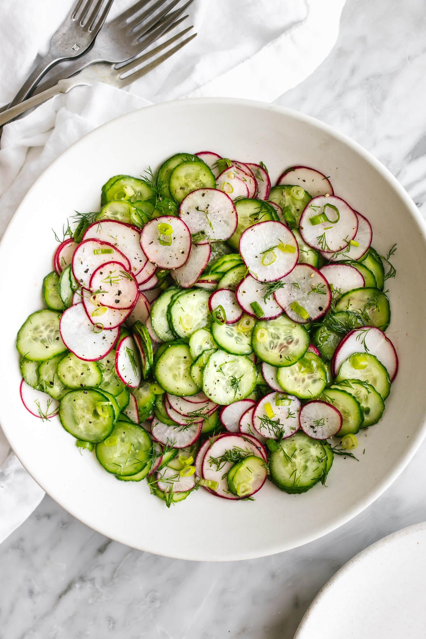 Eine weiße Schüssel Gurken-Radieschen-Salat neben Gabeln.