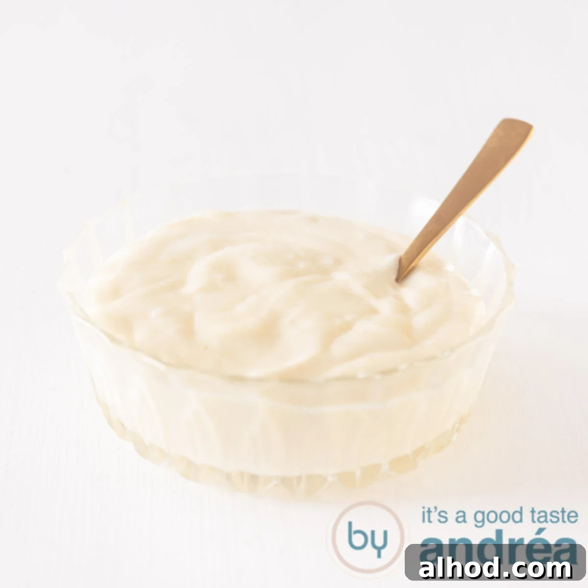 5 Homemade Sauces for the Ultimate Raclette Experience 3 A glass bowl filled with homemade mayonnaise on a white background. A golden spoon stands in the sauce