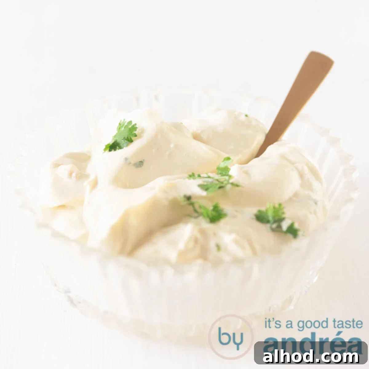 5 Homemade Sauces for the Ultimate Raclette Experience 7 A bowl filled with homemade garlic sauce, aioli, on a white background. A golden spoon stands in the bowl