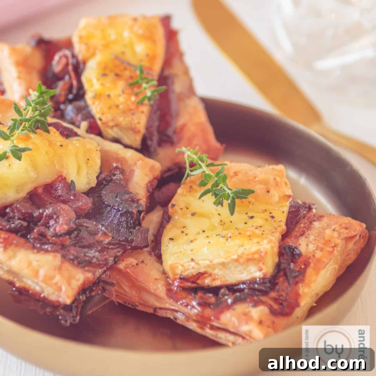 A square photo of puff pastry snacks with red onion, brie and bacon