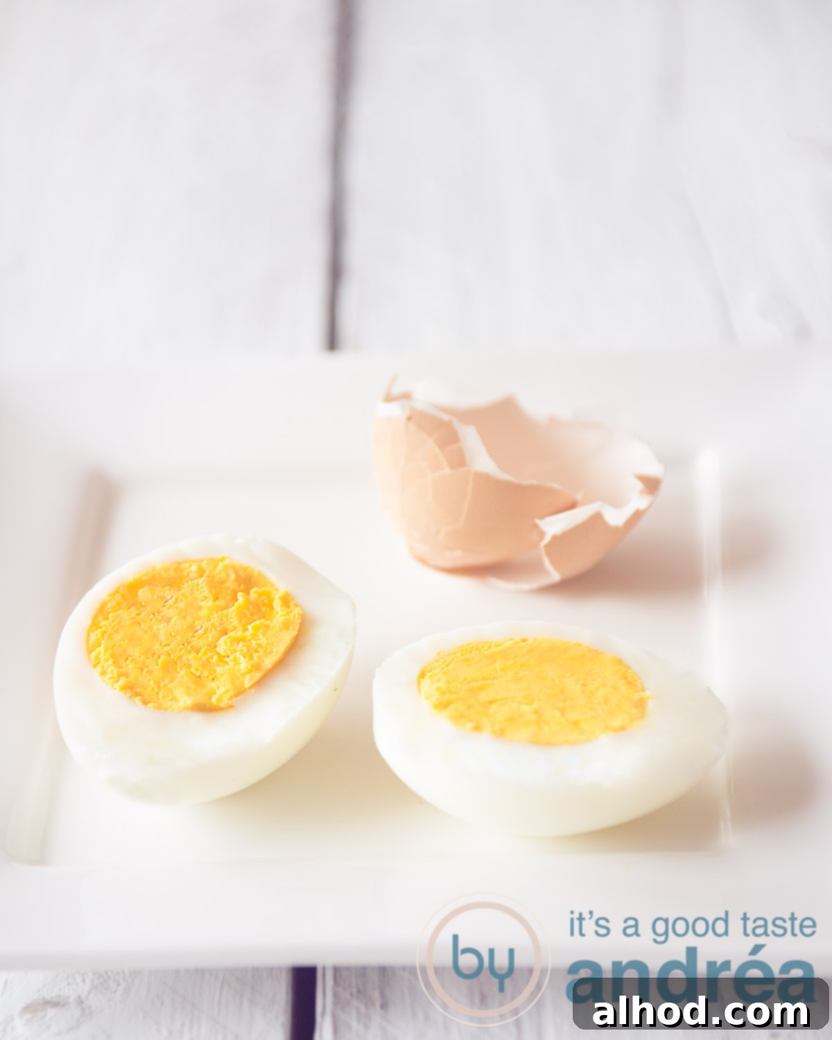 Mastering Hard and Soft Boiled Eggs 6 A hard-boiled egg, halved some egg shell in the back on a white background