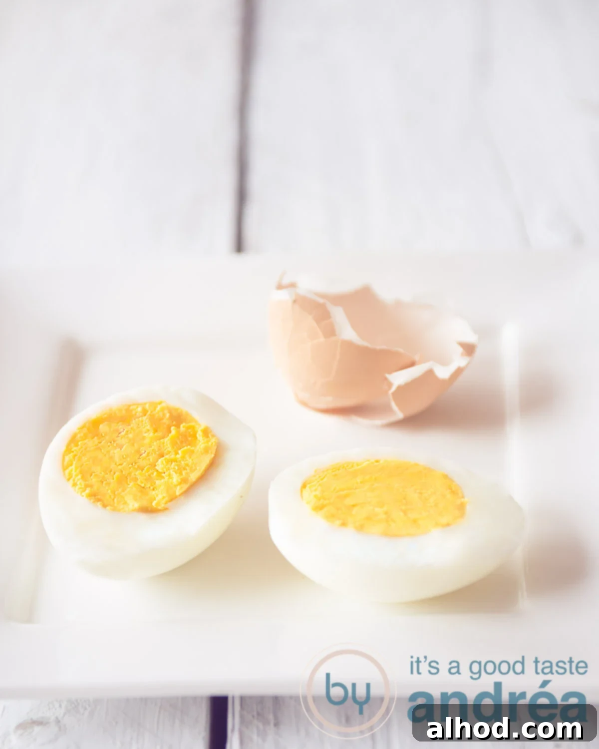 Perfect Eggs From Runny to Firm 6 A perfectly hard-boiled egg, halved, revealing a firm yellow yolk, with some shell fragments in the background on a white surface.