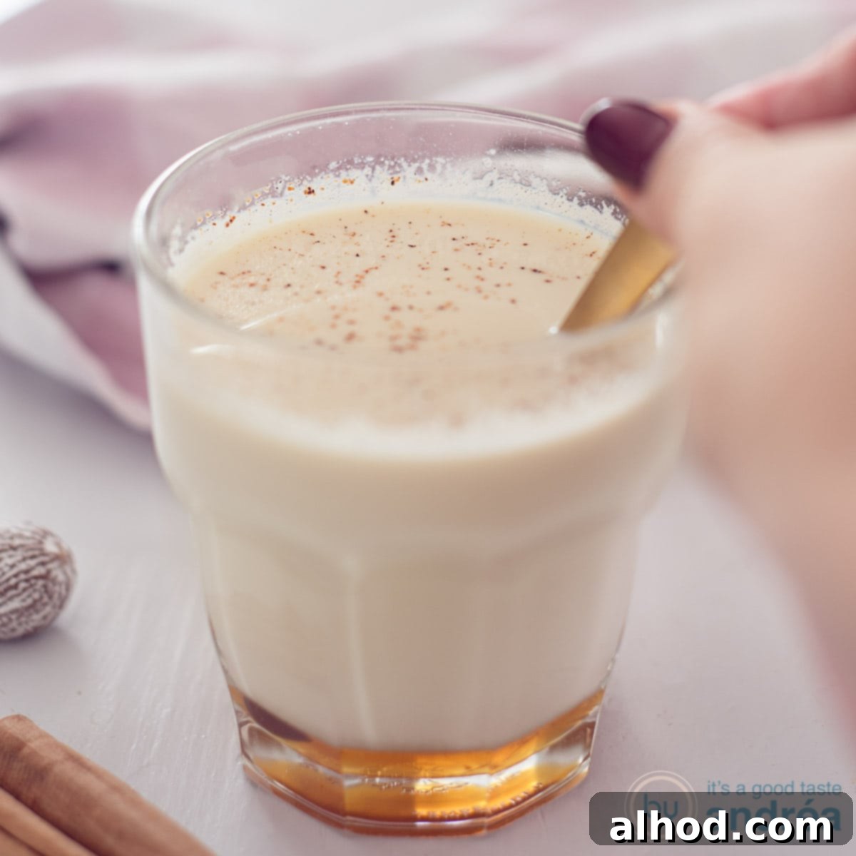 11 Merry & Bright Holiday Sips 8 A square photo with a glass in the middle filled with chai tea with milk and honey. A golden spoon stirs the glass.
