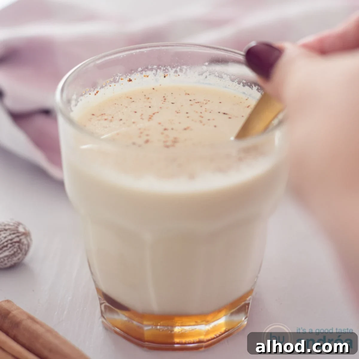 11 Festive Sips to Brighten Your Christmas 2 A square photo with a glass in the middle filled with chai tea with milk and honey. A golden spoon stirs the glass.