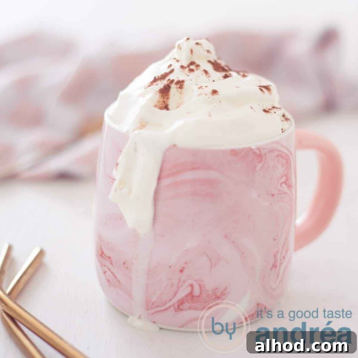11 Festive Sips to Brighten Your Christmas 7 A square photo of a pink mug of Baileys with hot chocolate and a whipped cream topping. A white background, in the background a pink and white tea towel. In the front left two gold straws