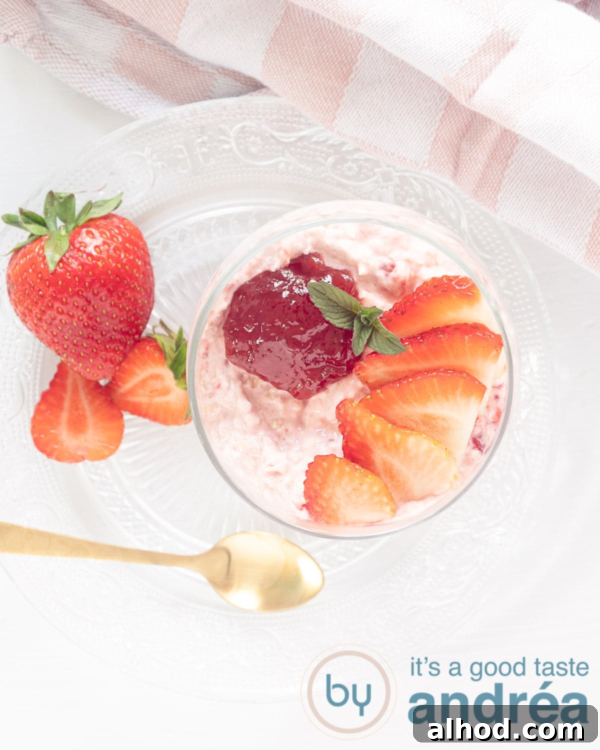 Creamy Strawberry Oat Smoothie Bowl 2 A photo from above of a Summer Strawberry smoothie in a bowl with a strawberry and jam topping. A white background and a golden spoon