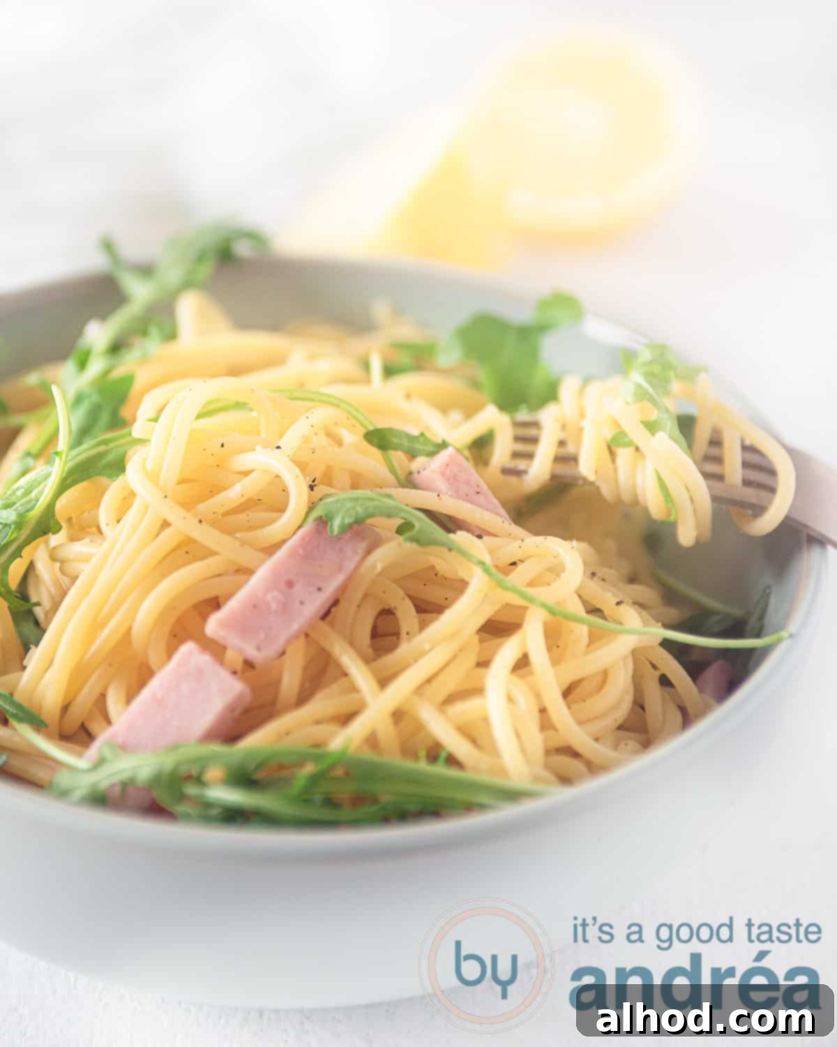 Hearty Italian Ham Spaghetti 5 A white bowl showcasing spaghetti, vibrant arugula, and briny capers, highlighting the fresh ingredients.