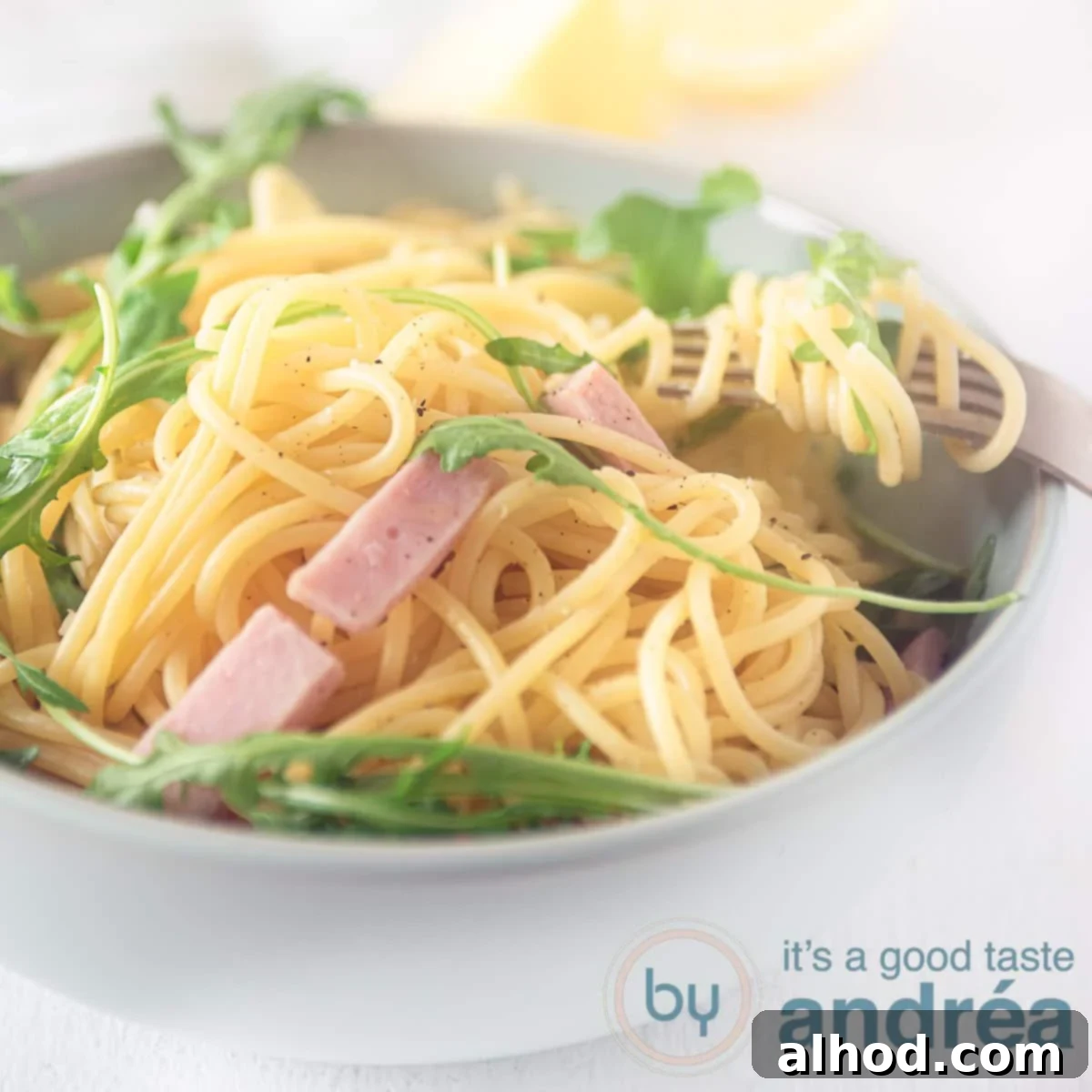 Hearty Italian Ham Spaghetti 6 A square photo of a gray bowl filled with ham, arugula, and spaghetti on a white background, garnished with a sprig of basil.