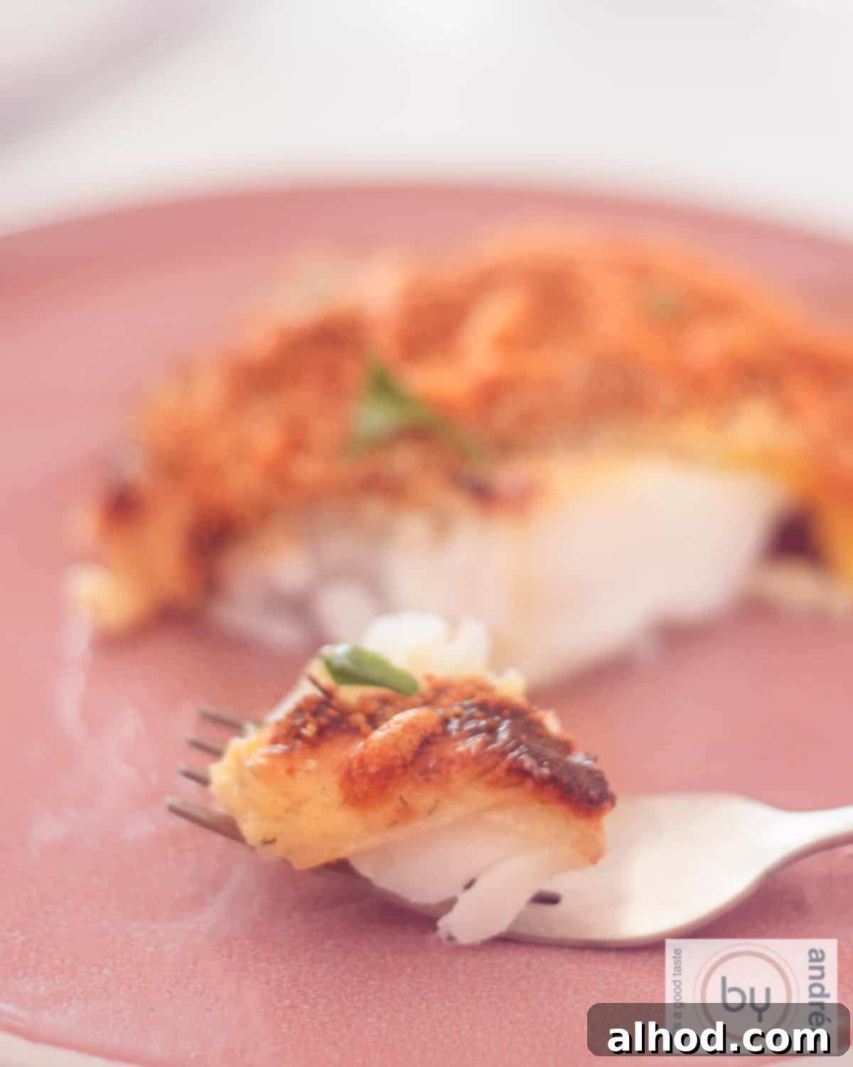 Effortless Cheesy Cod Bake 2 A beautifully baked cod fillet with a golden, crispy cheesy topping, served in a white casserole dish. A fork is taking a bite from the flaky fish, showcasing the tender interior.