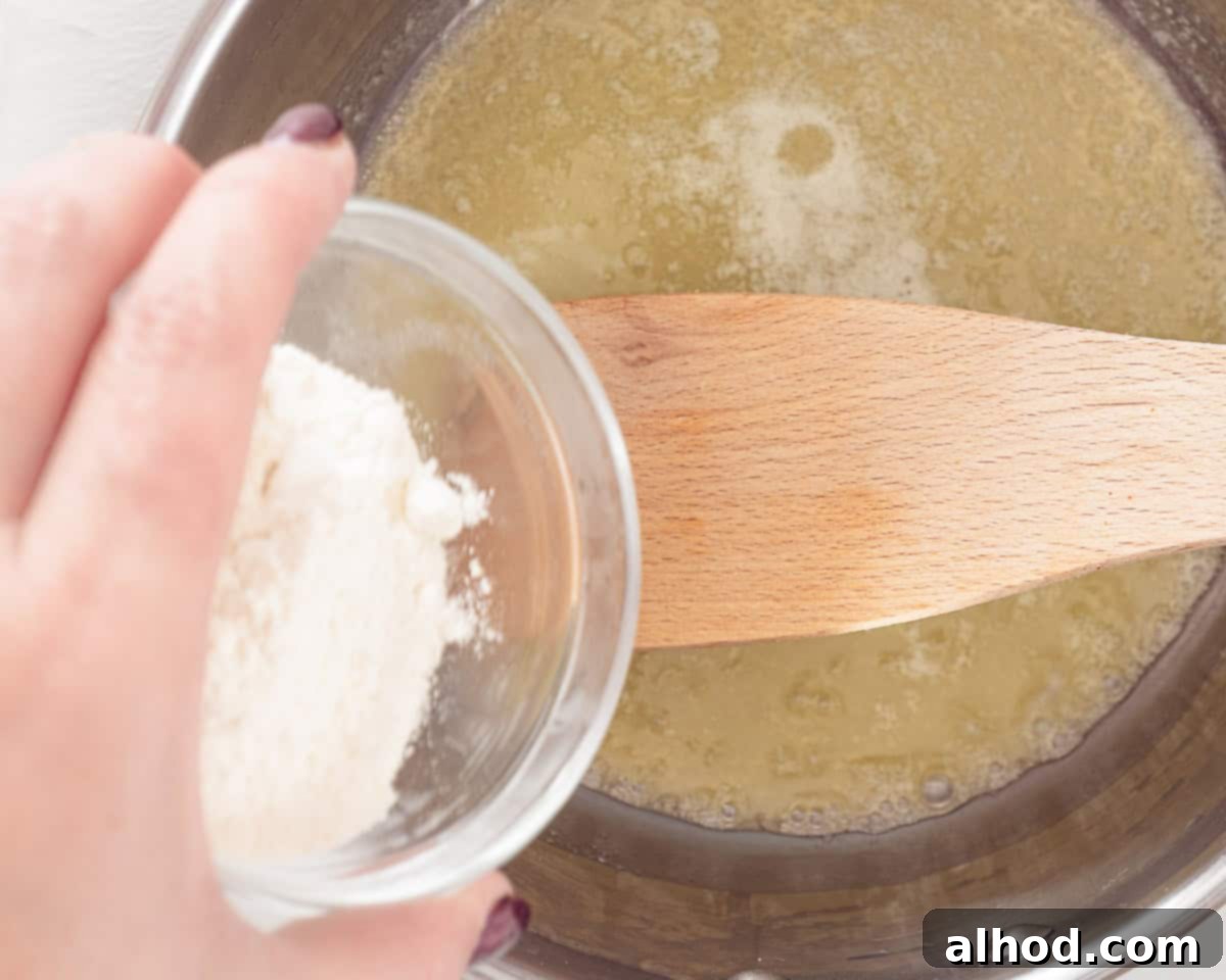 Effortless Cheesy Cod Bake 4 A saucepan on a stovetop with melted butter and flour, being stirred with a whisk to create a roux, the base for the creamy sauce.