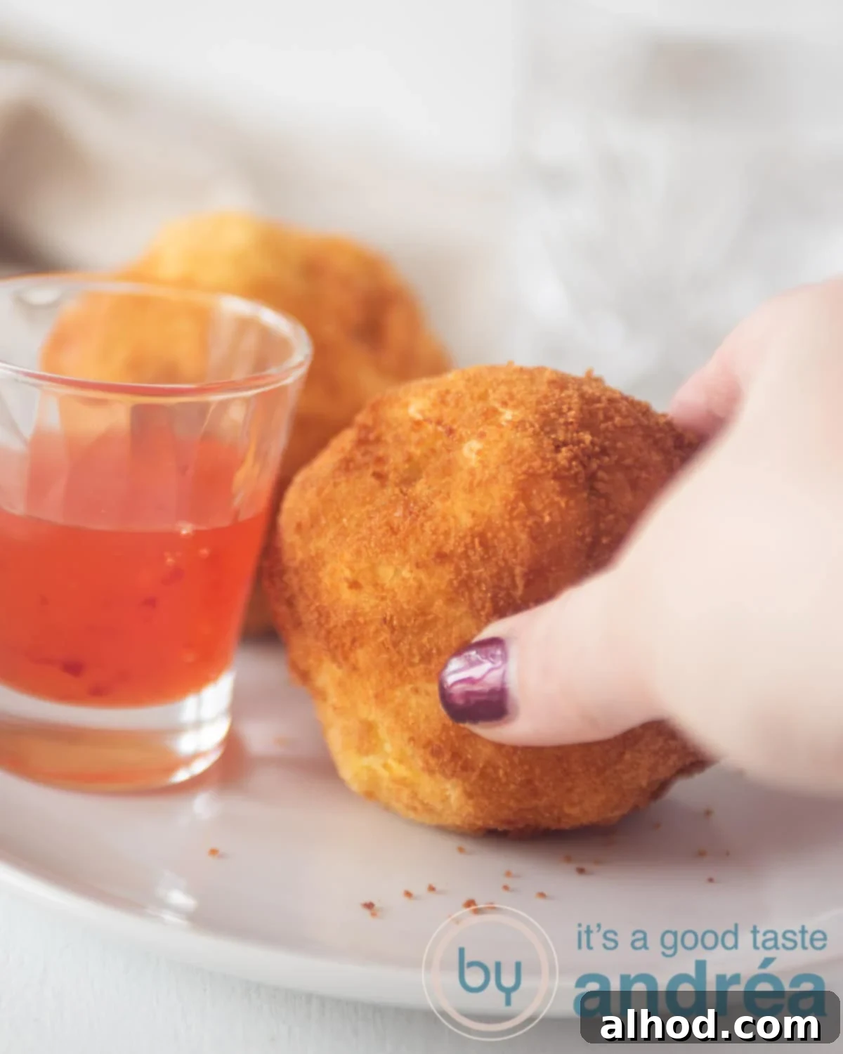 Homemade Beef Papa Rellena 2 A hand picking a papa rellena from a white plate. Some chili sauce in a glass