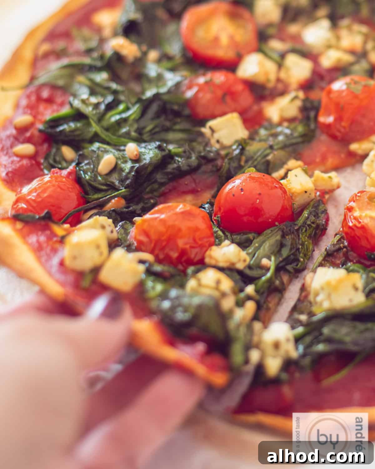 Artisan Spinach Feta Pizza with Garden Tomato Sauce 3 A slice of pizza with spinach, feta, pine nuts, and tomatoes. A slice is taken out.
