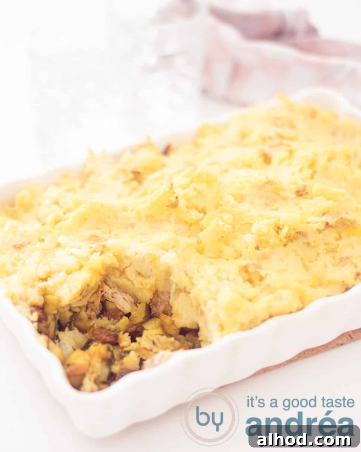 Smoked Mackerel and Zucchini Potato Bake 2 An elevation shot showing a white casserole covered in mashed potatoes, with a bite removed, revealing the zucchini, raisins and smoked mackerel filling.