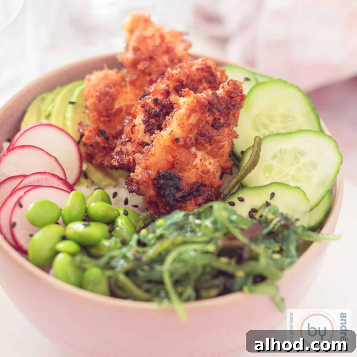 25-Minute Crispy Sriracha Chicken Sushi Bowl 4 Square photo of a pink bowl with sushi bowl ingredients: crispy sriracha chicken, seaweed salad, edamame beans, radish, and cucumber.