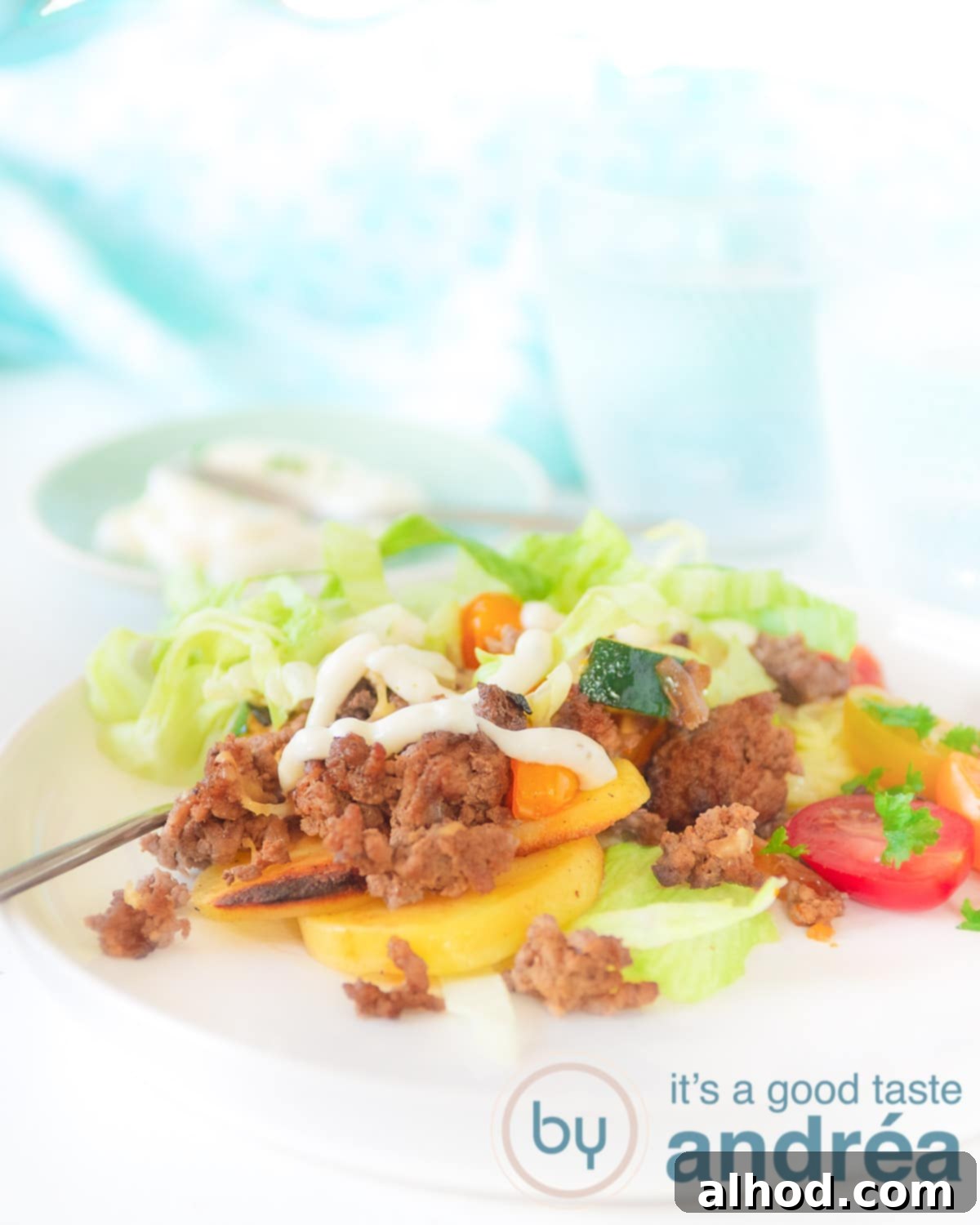 Kapsalon: A Healthy Makeover 3 A white plate with perfectly cooked, healthy Kapsalon featuring crispy baked potatoes, savory minced beef, fresh iceberg lettuce, and a drizzle of garlic sauce.