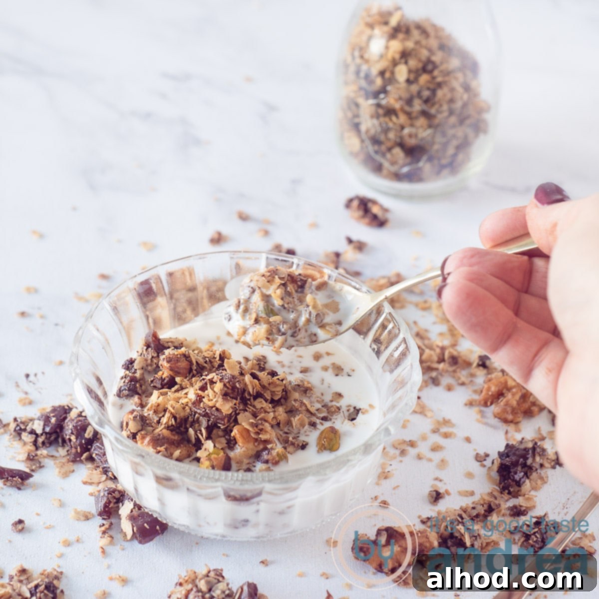 A glass bowl filled with creamy yogurt and crunchy dark chocolate granola, with a golden spoon taking a bite.