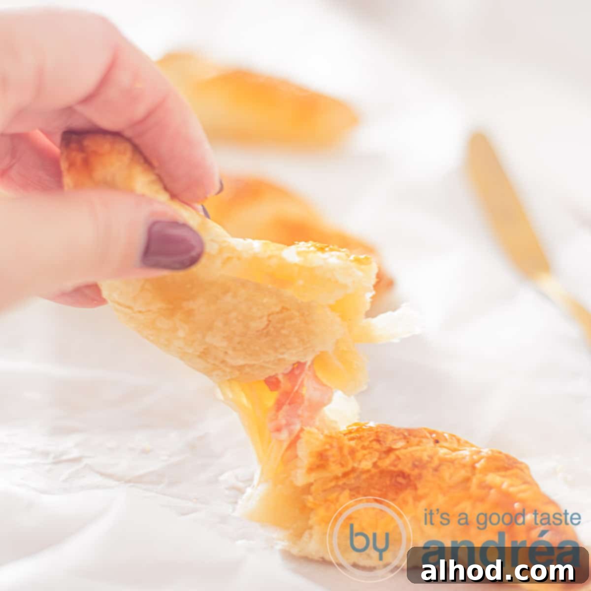 Three golden-brown ham and cheese puff pastry croissants, with one broken open to reveal melted cheese and ham.