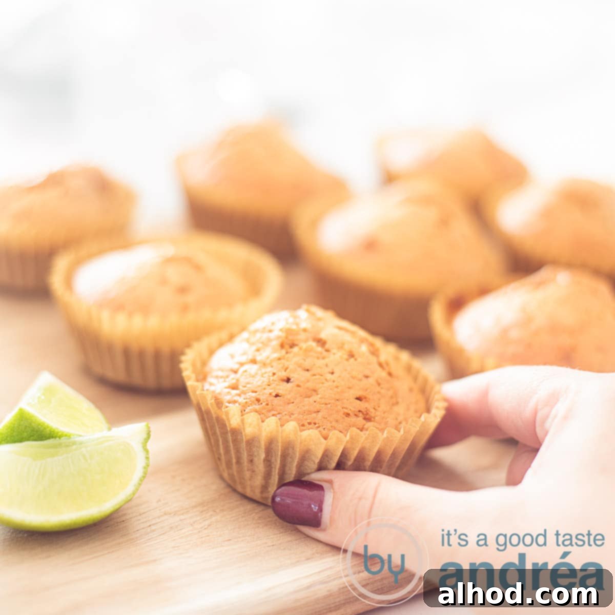 A wooden board showcasing a selection of beautifully baked lime muffins, with a hand reaching for one.