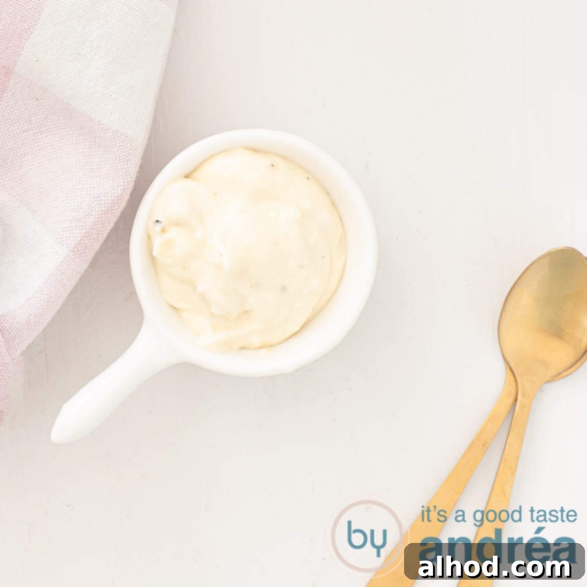 Upgrade Your Mayo: 5 Delicious Flavor Infusions 16 A square photo with a spoonful of garlic mayonnaise, two golden spoons on the side and a pink checkered tea towel in the top right, white background.