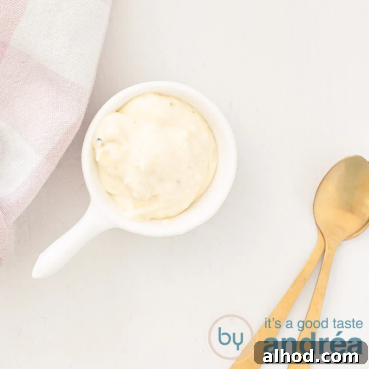 Spice Up Your Mayo 5 Creative Recipes 16 A square photo with a spoonful of garlic mayonnaise, two golden spoons on the side and a pink checkered tea towel in the top right, white background.