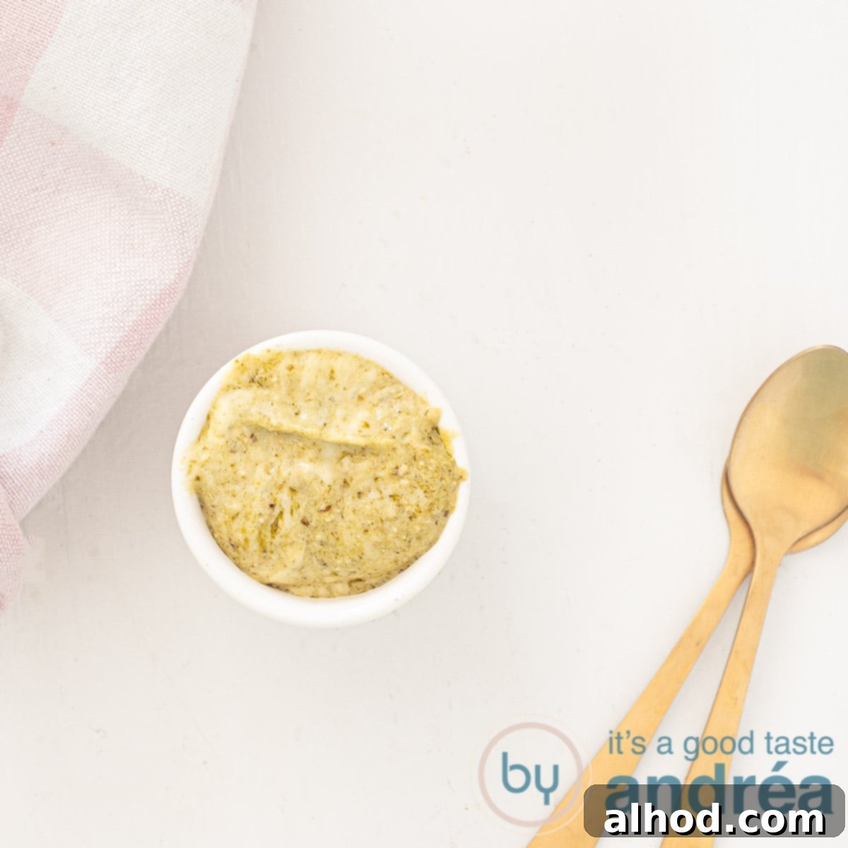 Upgrade Your Mayo: 5 Delicious Flavor Infusions 18 A square photo with a spoon of pesto mayonnaise, two golden spoons on the side and a pink checkered tea towel in the top right, white background.