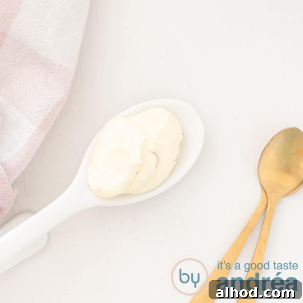 Upgrade Your Mayo: 5 Delicious Flavor Infusions 20 A square photo with a spoon of saffron mayonnaise, two golden spoons on the side, a pink checkered tea towel at the top right, white background.