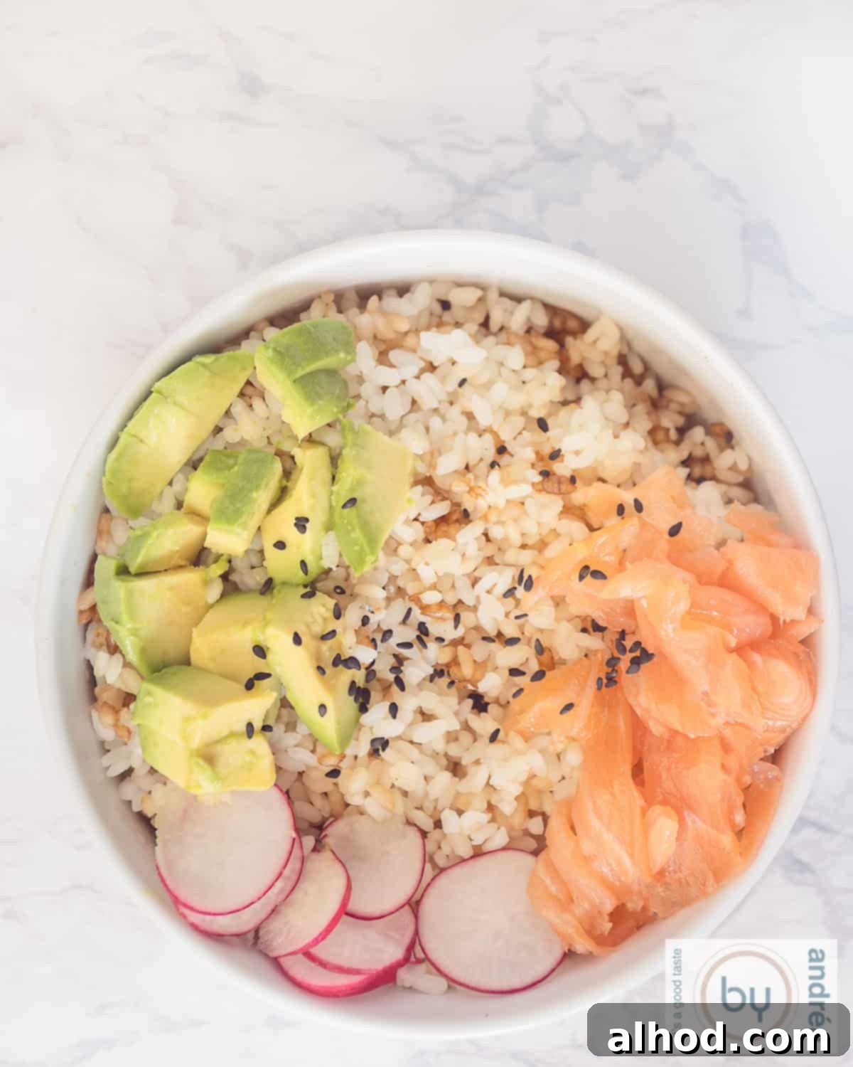 Simple Smoked Salmon Sushi Bowl Recipe 3 A top-down photo of a white bowl on a marble surface, filled with sushi rice, radish, avocado, salmon, and sesame seeds.