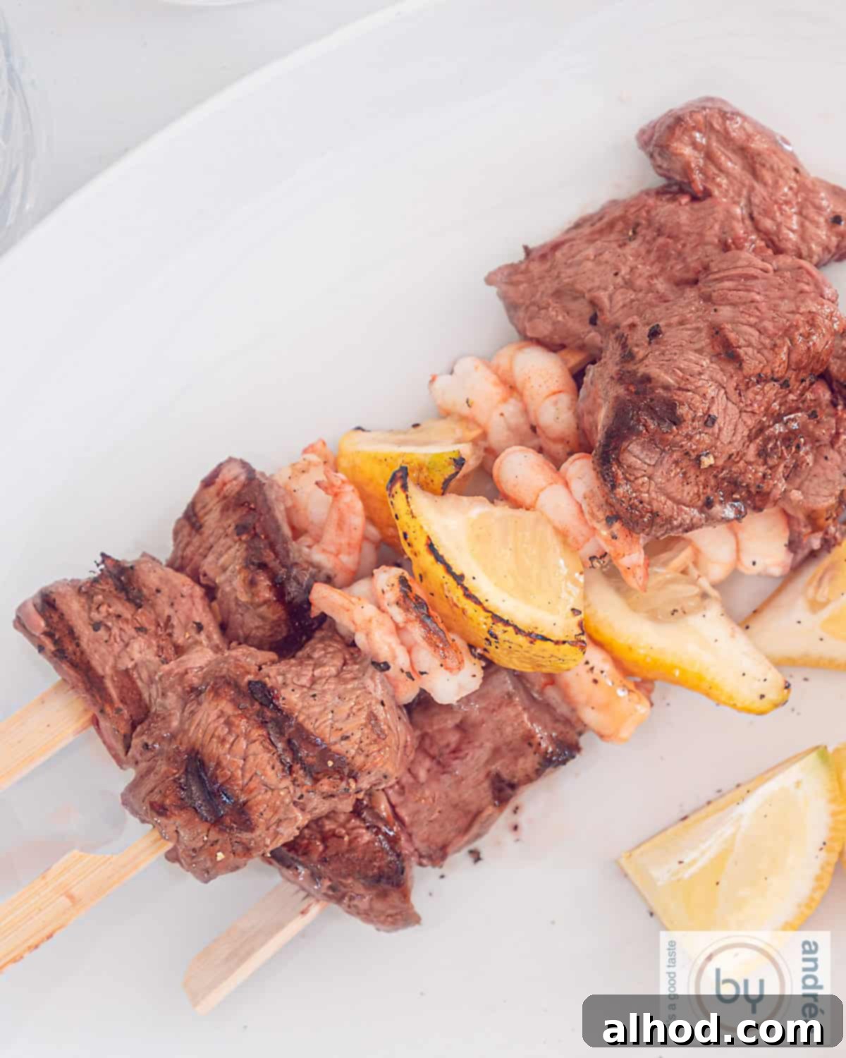Grilled Surf and Turf Skewers 3 A top-down photo featuring three perfectly grilled surf and turf skewers on a white plate, highlighting the steak, shrimp, and lemon.
