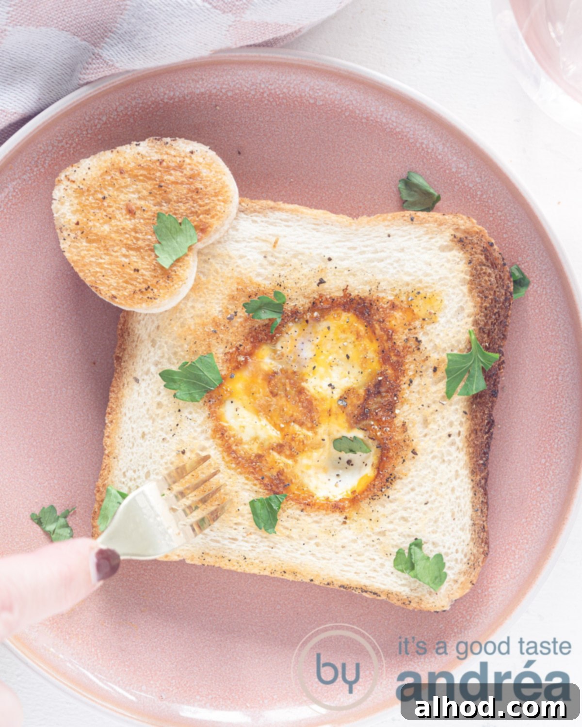 Valentines Day Egg in a Hole 2 A top-down photo of a pink plate on a white background featuring a perfectly cooked heart-shaped egg-in-a-hole toast, ready for a romantic Valentine's Day breakfast.