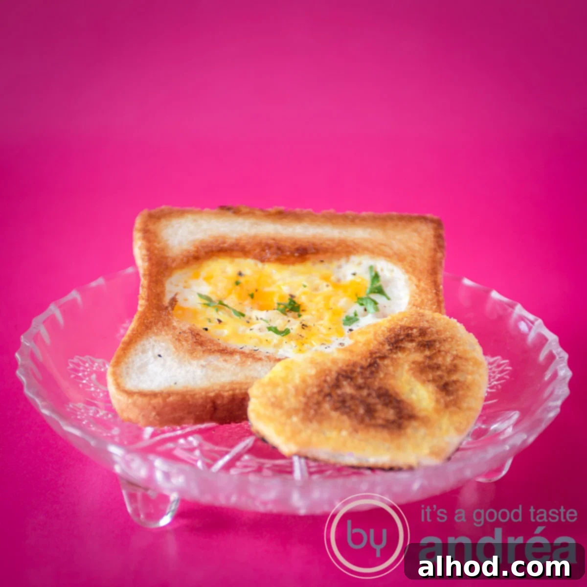 Valentines Day Egg in a Hole 6 A square photo with a pink background a glass plate topped with a egg-in-a-hole sandwich, heart shaped