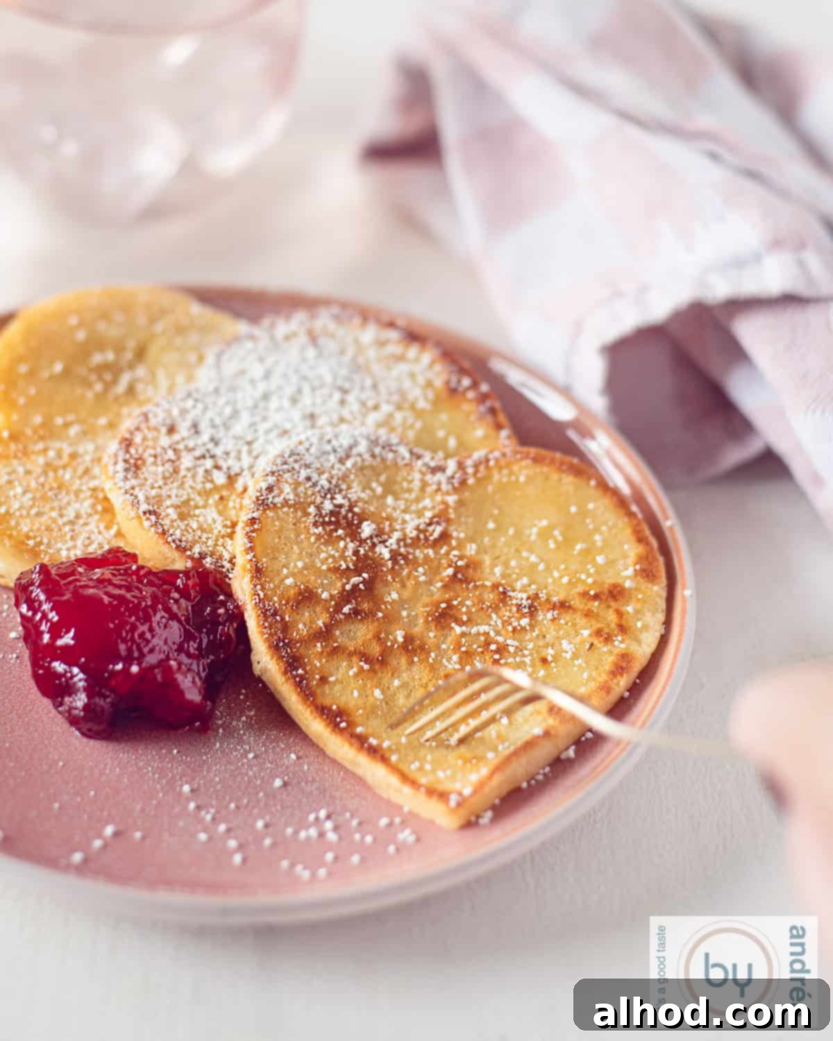 Sweetheart Pancakes with Strawberry Delight 2 A height photo of a pink plate with heart-shaped pancakes and strawberry jam. A fork is poking a pancake.