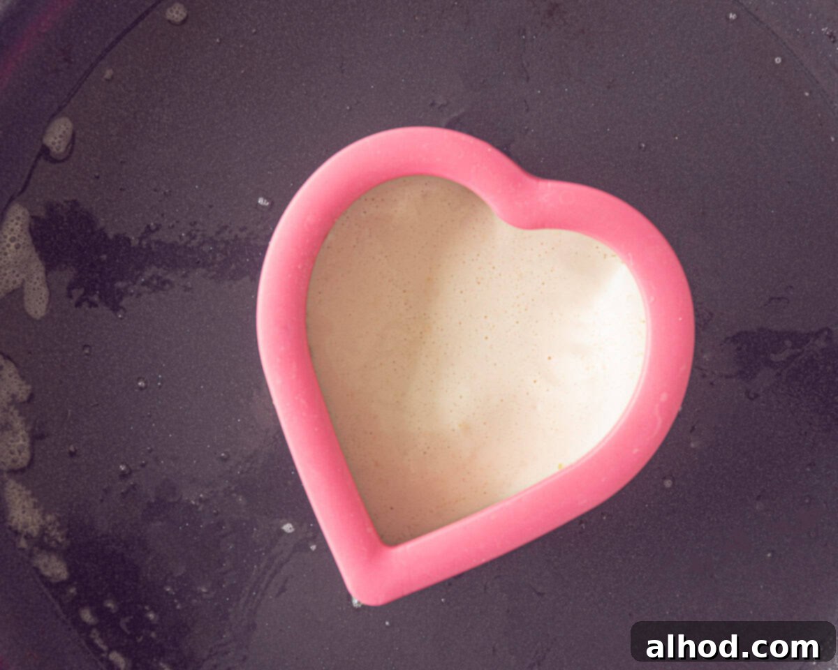 Sweetheart Pancakes with Strawberry Delight 6 A heart-shaped cookie cutter in a frying pan with batter in it.