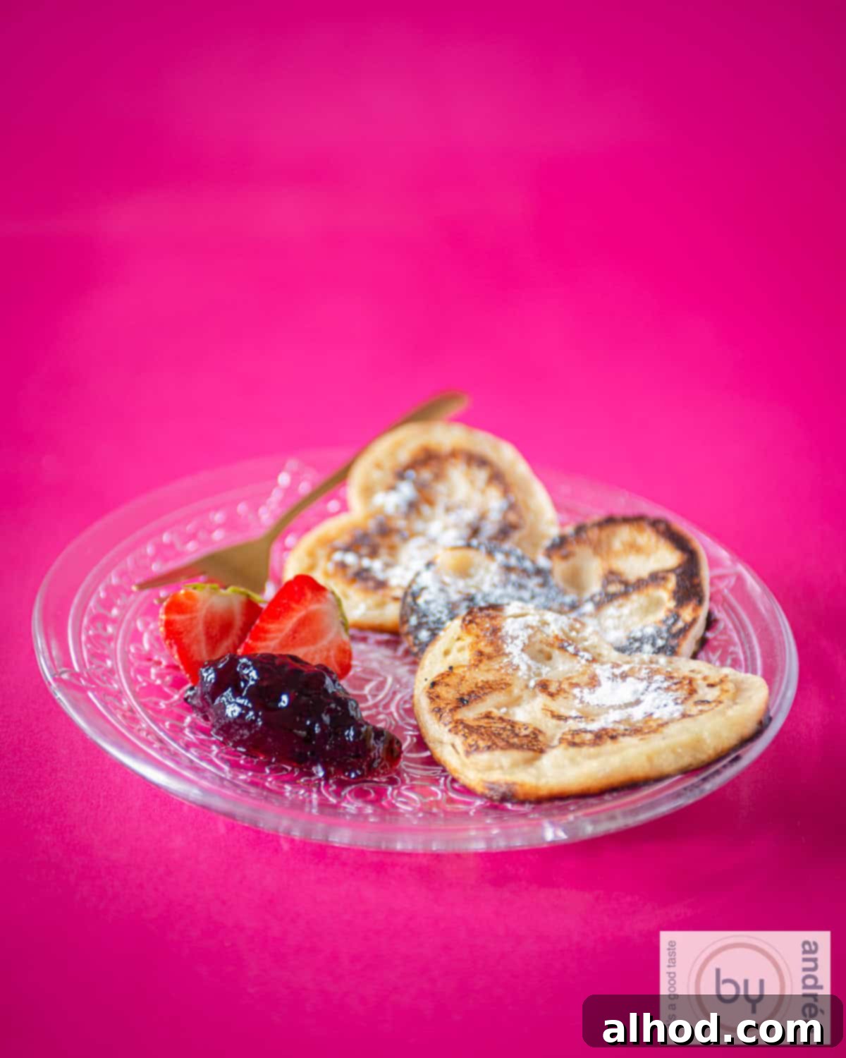 Sweetheart Pancakes with Strawberry Delight 8 An aerial photo of a glass plate with heart-shaped pancakes, strawberries and jam. A pink background