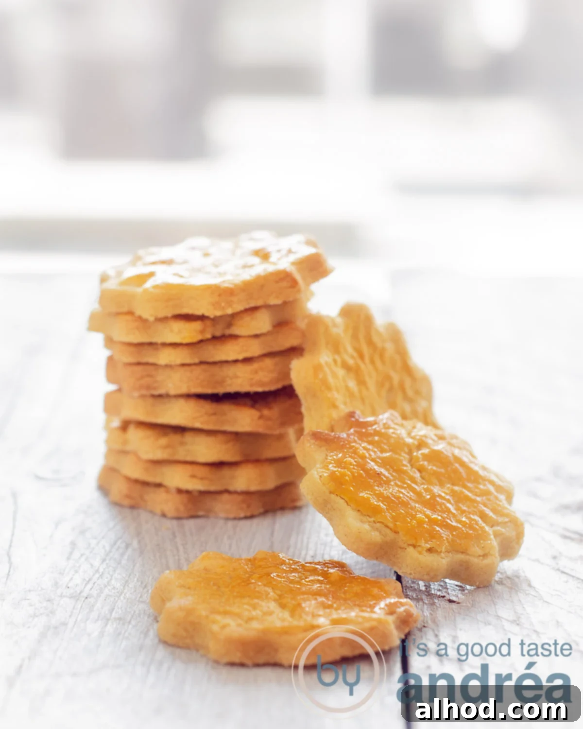 Delicate French Butter Sables 2 A stack of golden brown sable cookies, with two more cookies artfully leaning against the stack. A single, perfectly baked cookie rests in the foreground, ready to be enjoyed. Everything is presented on a rustic whitewash wooden board, highlighting the simple elegance of these classic French butter treats.