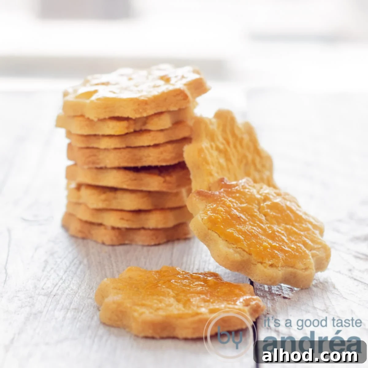 Delicate French Butter Sables 6 A square picture with a row of golden brown sable cookies on a white wooden plate. Some cookies are leaning against the stack, with a single, inviting sable cookie in front, highlighting their perfect texture and presentation.
