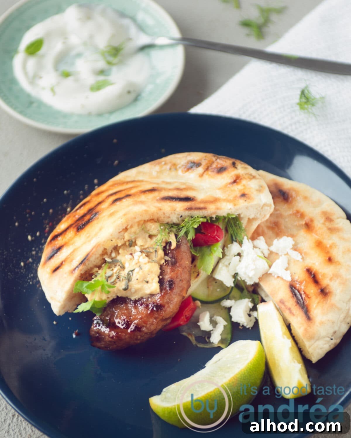 Mediterranean Feta Burgers Made Easy 6 A vibrant blue plate showcasing a Greek Feta burger in pita with grilled vegetables and crumbled feta cheese