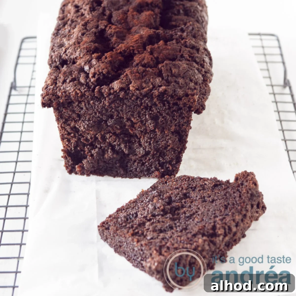 Decadent Dark Chocolate Zucchini Cake 6 A square photo of a Chocolate zucchini pound cake, one slice cut of laying in front on a baking paper on a rack.