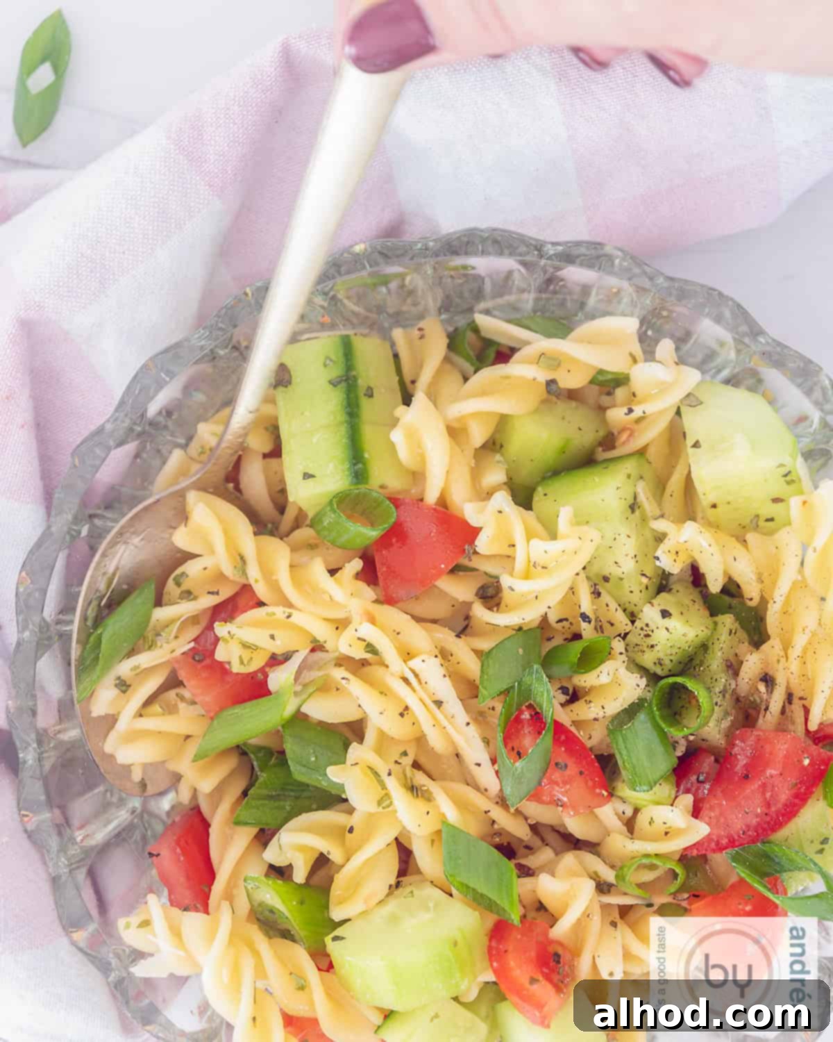 Zesty Italian Veggie Pasta Salad 2 A height picture top down of a glass bowl filled with pasta salad, italian dressing, cucumber, spring onions and tomatoes.