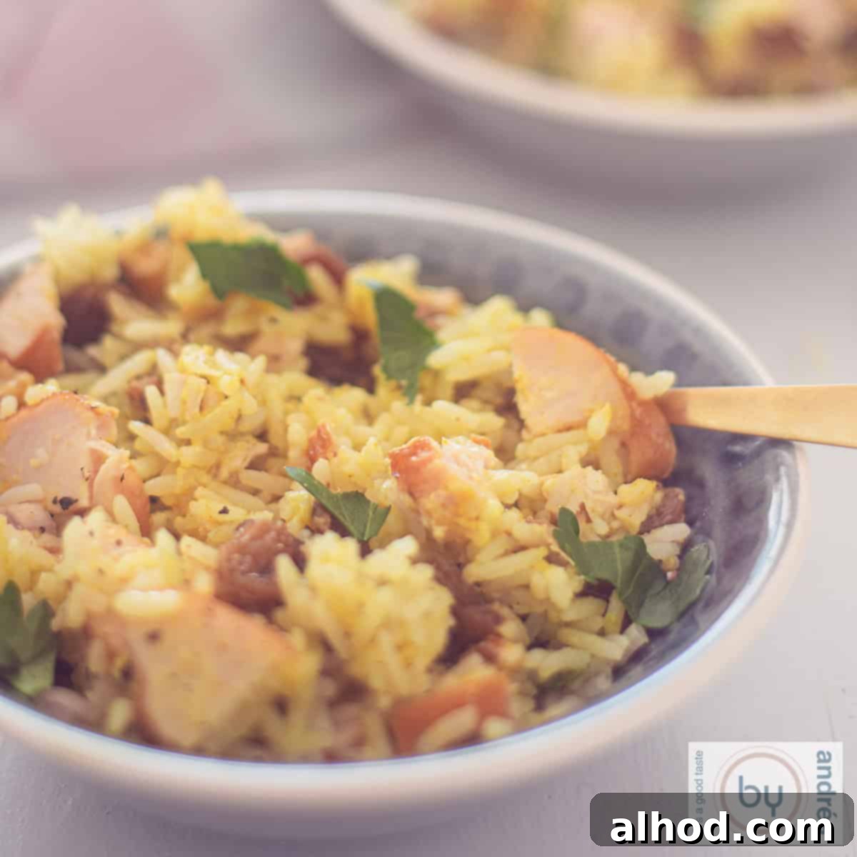 Golden Smoked Chicken and Curry Rice Medley 4 A square photo with a gray bowl filled with a rice salad with curry, smoked chicken, raisins and walnuts