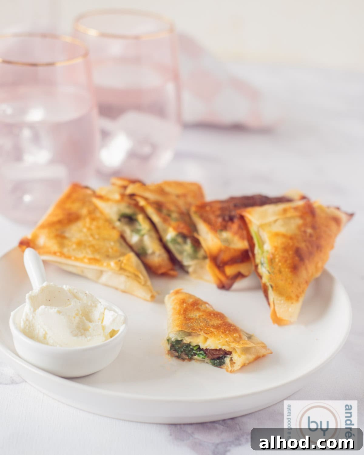Crispy Spinach and Feta Bites 2 An aerial shot of a white plate with a row of filo pastry filled with spinach snacks. A dip in the foreground and a snack, where you can see the filling.