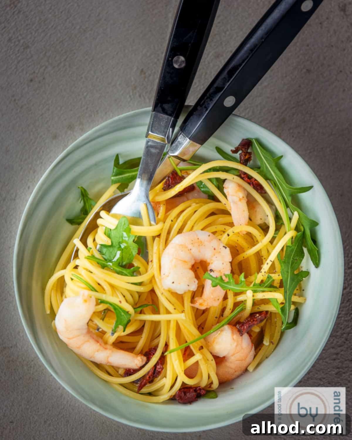 A top-down photo of a green bowl with spaghetti, arugula, and shrimp