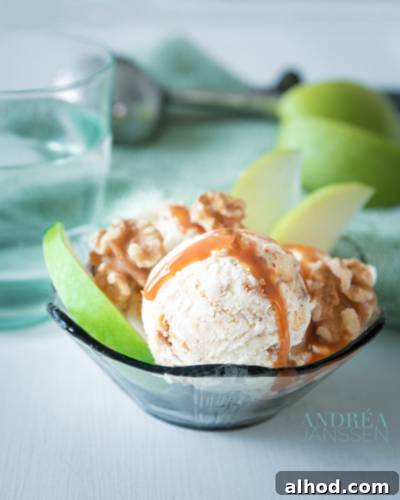 No-Fuss Apple Pie Ice Cream Dream 5 A elegant black glass bowl overflowing with creamy apple pie ice cream, beautifully garnished with crunchy walnuts, delicate slices of fresh apple, and a luxurious swirl of caramel sauce. In the soft-focus background, an ice cream scoop and a few more vibrant red apples complete the rustic-chic and inviting scene.