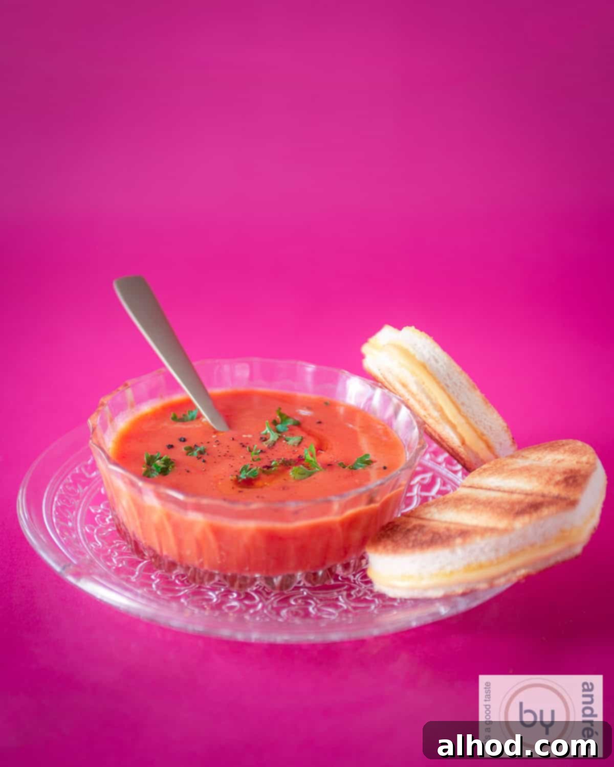 Herbed Tomato Soup and Gooey Grilled Cheese 3 A height photo with a pink background, a glass plate with a glass bowl of rich tomato soup and heart-shaped toasted sandwiches, perfect for a special occasion.