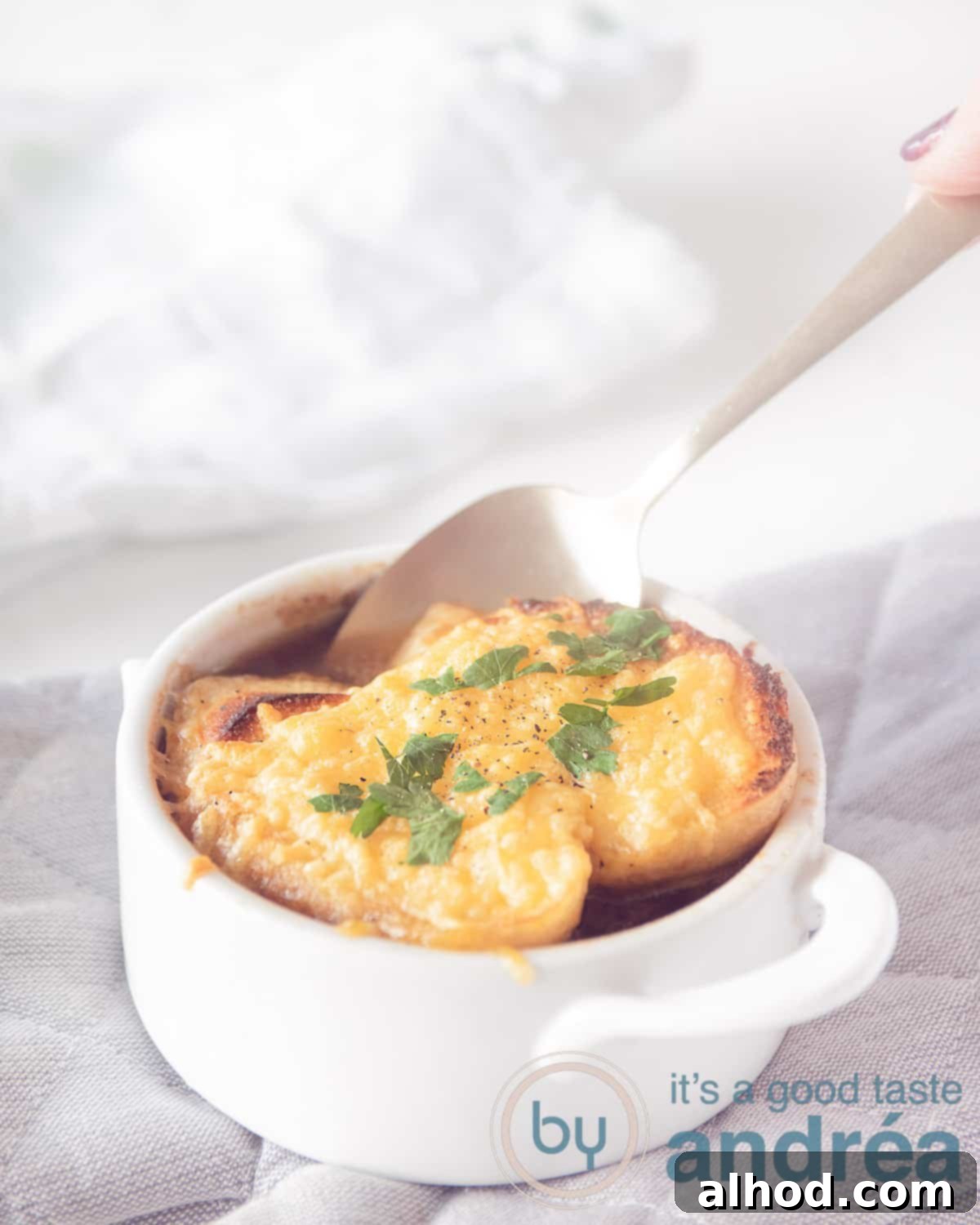 Hearty Red Onion Soup with Cheesy Toast 2 A white bowl of classic French Onion Soup topped with two pieces of golden-brown French bread au gratin. A golden spoon is poised, ready to take a delicious bite of the rich, savory soup and cheesy bread.