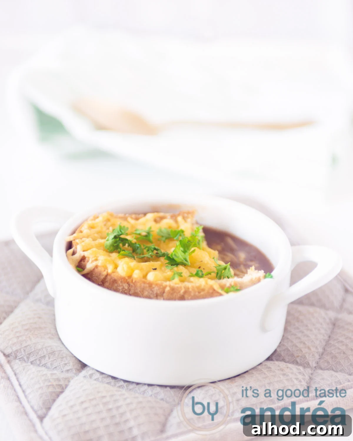Hearty Red Onion Soup with Cheesy Toast 5 A close-up of a white bowl filled with French onion soup, elegantly topped with a grilled cheese baguette, featuring bubbling, melted Gruyère cheese and fresh parsley garnish.
