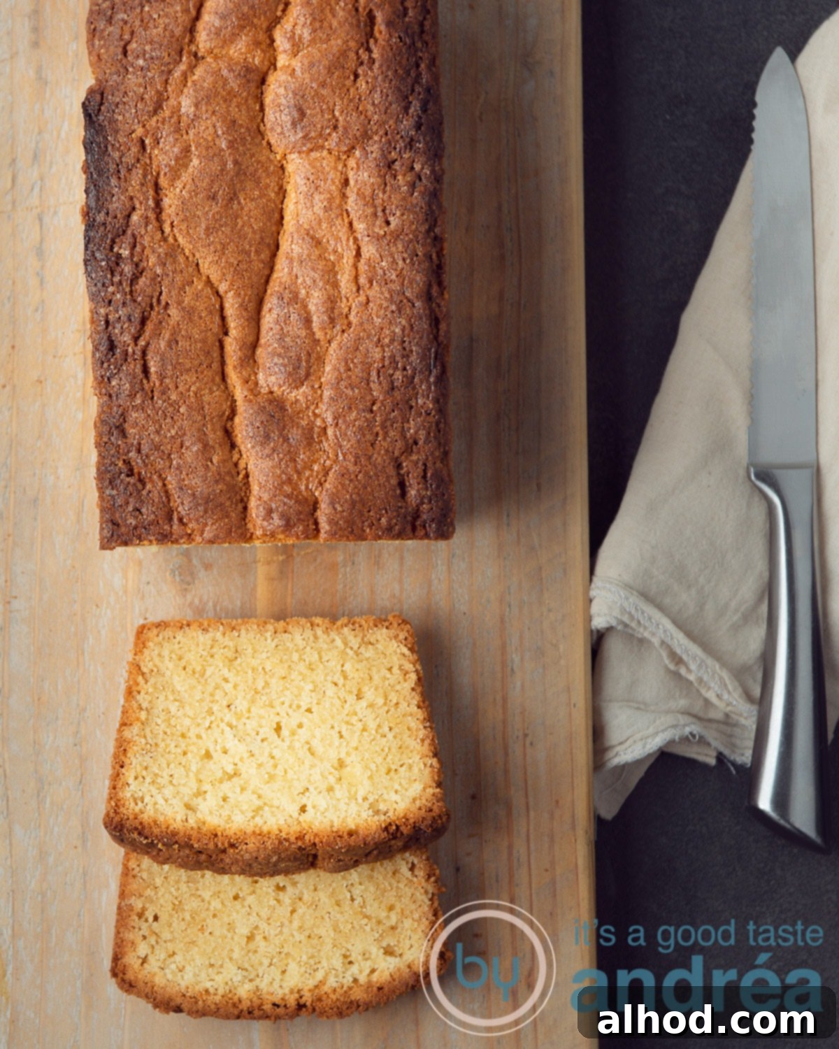 Golden Dutch Pound Cake 2 A golden-brown Dutch pound cake on a rustic wooden board with two slices cut, revealing its moist interior. A brown linen cloth and a silver knife are placed to the right.