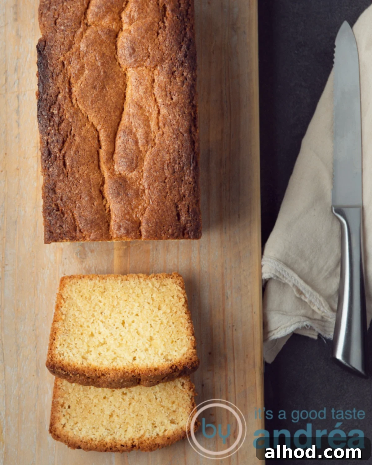 A beautifully baked Dutch pound cake on a wooden board, with two slices already cut. A brown cloth and a knife are placed beside it.
