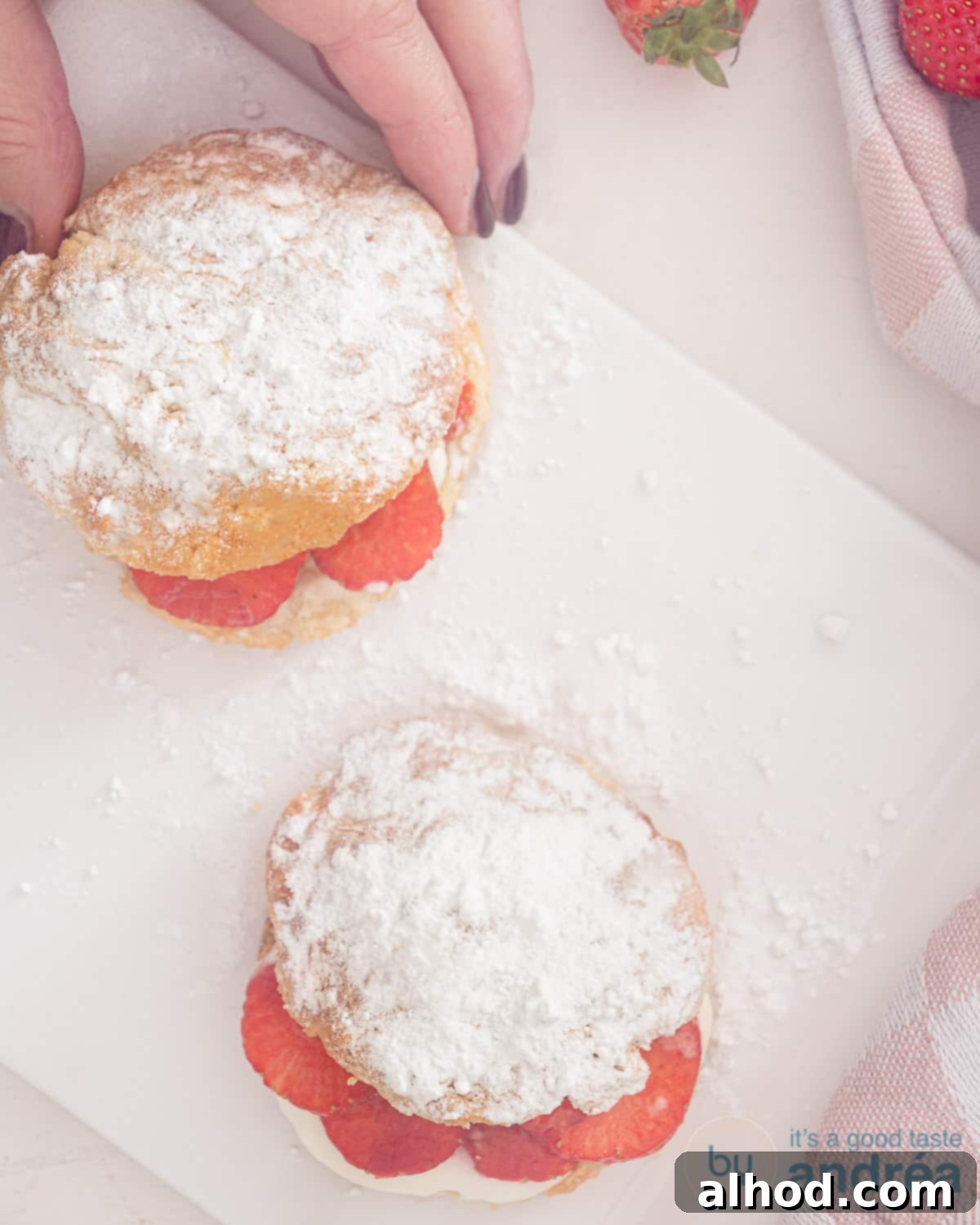 Strawberry and Cream Scones 2 A photo from above of two scones on a white plate. A hand taking a scone from the plate
