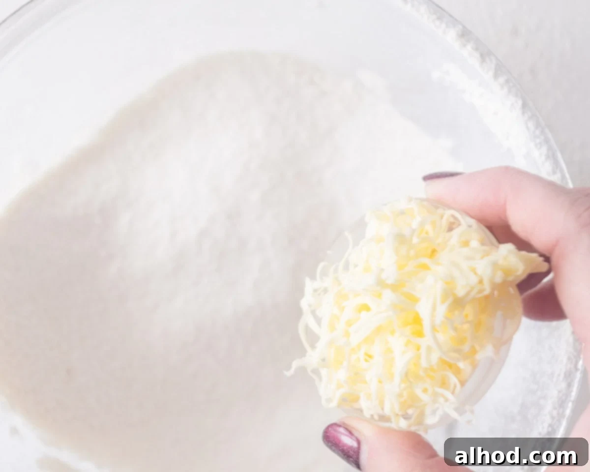 Grated frozen butter is added to the dry ingredients in a glass bowl.