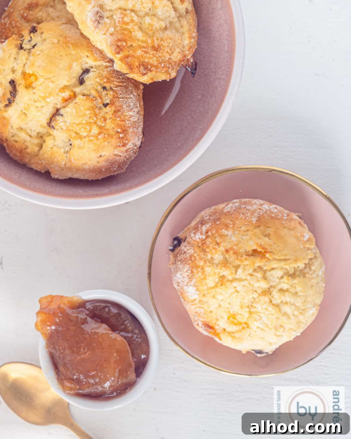 A height picture, top down, a pink plate with an orange scone, some orange jam and a pink bowl with more scones.